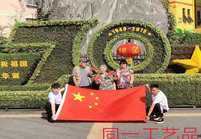 北京游客在植物綠雕國(guó)慶綠雕前舉國(guó)旗合影